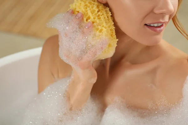 Woman with sponge taking bubble bath, closeup