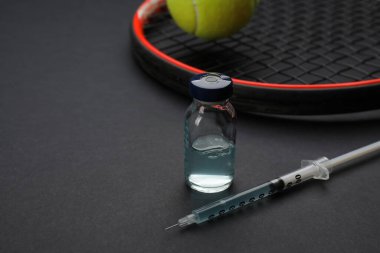 Siyah arka planda topu olan tenis raketinin yanında şişe ve şırınga. Mesaj için yer var. Doping kavramı