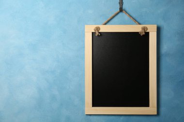 Açık mavi duvarda asılı temiz küçük siyah karatahta, metin için boşluk