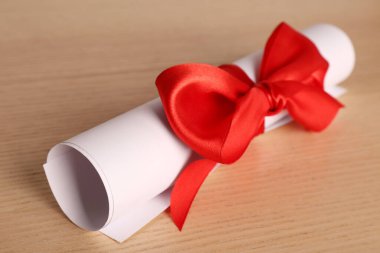 Mezuniyet diploması, ahşap masada kırmızı kurdeleyle bağlanmış, yakın plan.