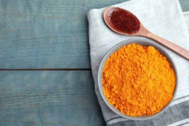 Bir kase safran tozu ve kaşık açık mavi ahşap masa üzerinde kurumuş çiçek lekeleri, düz uzanmış. Metin için boşluk