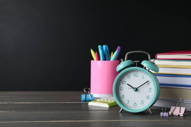 Alarm saati ve tahtanın yanındaki ahşap masada farklı kırtasiye malzemeleri. Mesaj için yer var. Okul zamanı.