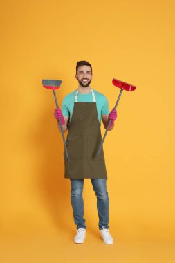 Turuncu arka planda süpürge ve faraş olan adam.