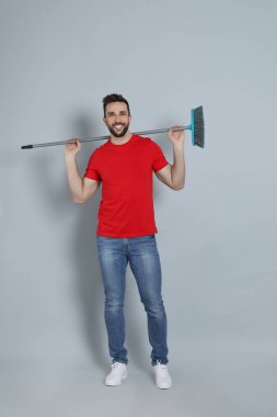 Gri arka planda süpürgesi olan yakışıklı bir adam.