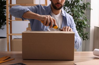 İçerideki ahşap masada paket açmak için bıçak kullanan adam, yakın plan.