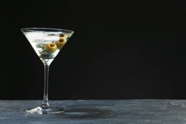 Gri masadaki buzlu ve zeytinli martini kokteyli koyu arka planda. Metin için boşluk