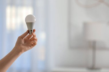 Arka planda floresan ampulü tutan bir kadın, mesaj için yere yakın çekim yapıyor. Enerji tasarrufu kavramı