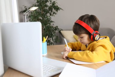 Modern dizüstü bilgisayarı olan sevimli küçük çocuk evde online çalışıyor. E-öğrenme