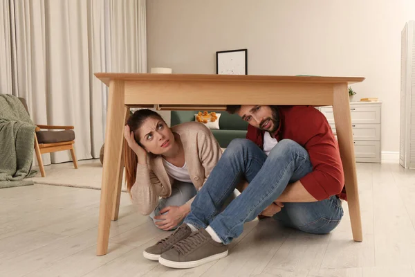 地震の間テーブルの下に隠れて怖いカップル — ストック写真