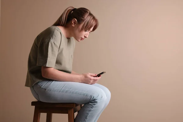 Jovem Com Postura Usando Smartphone Enquanto Sentado Banquinho Contra Fundo — Fotografia de Stock