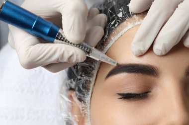 Salonda kalıcı kaş makyajı yapılan genç bir kadın, yakın plan.