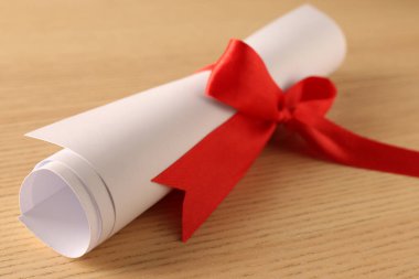 Mezuniyet diploması, ahşap masada kırmızı kurdeleyle bağlanmış, yakın plan.
