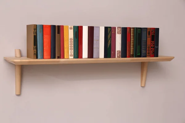 Wooden shelf with different books on light wall