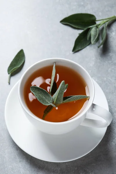 一杯芬芳的鼠尾草茶和鲜叶放在灰色的桌子上 — 图库照片