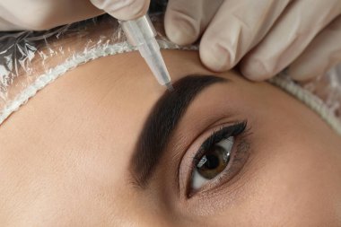 Salonda kalıcı kaş makyajı yapılan genç bir kadın, yakın plan.