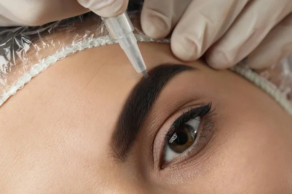 Salonda kalıcı kaş makyajı yapılan genç bir kadın, yakın plan.