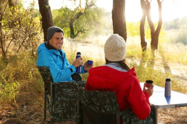 Çift kamp sandalyelerinde dinleniyor ve dışarıda sıcak içkinin tadını çıkarıyor.