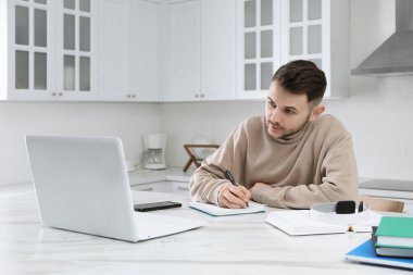 Genç adam mutfakta çalışmak için modern dizüstü bilgisayar kullanıyor. Uzaklık öğrenimi