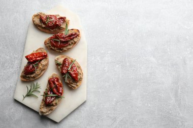 Lezzetli ezmeli ekmek dilimleri, güneşte kurutulmuş domates ve açık gri masada biberiye, üst manzara. Metin için boşluk