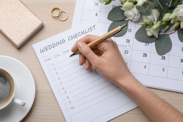 女性は木製のテーブルで結婚式のチェックリストを記入 トップビュー — ストック写真