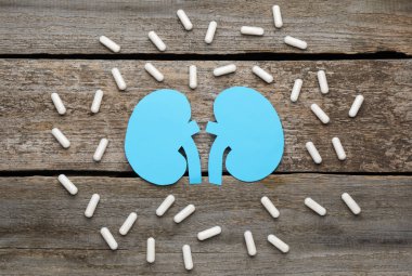 Böbrek ve haplardan yapılmış kağıt kesiği. Tahta masanın üzerinde, düz yerde.