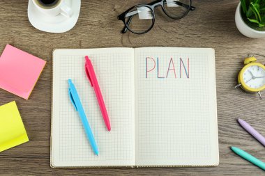 Kelime planlı defter, kahve, çalar saat, gözlük ve kırtasiye ahşap masa, düz yatıyordu.