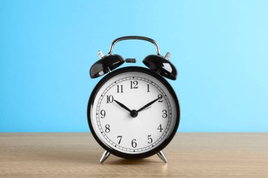 Açık mavi arkaplana karşı ahşap masada siyah alarm saati