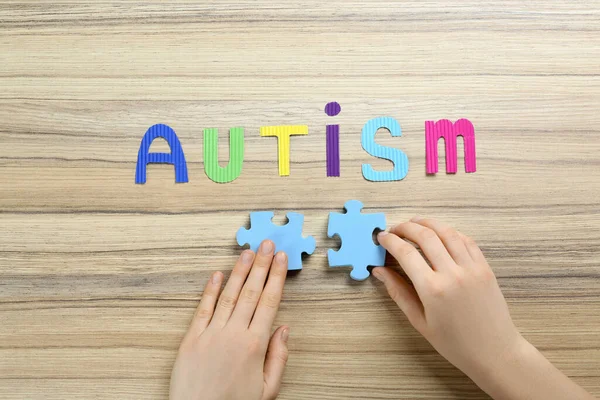 Vrouw Elkaar Puzzelstukjes Onder Woord Autisme Houten Tafel Bovenaanzicht — Stockfoto