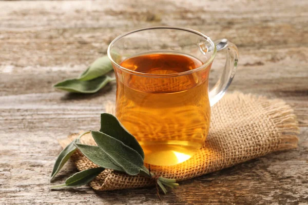 木のテーブルの上で香り豊かなセージ茶と新鮮な葉のカップ — ストック写真