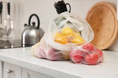 Mutfaktaki beyaz tezgahta farklı taze ürünlerin olduğu plastik torbalar.