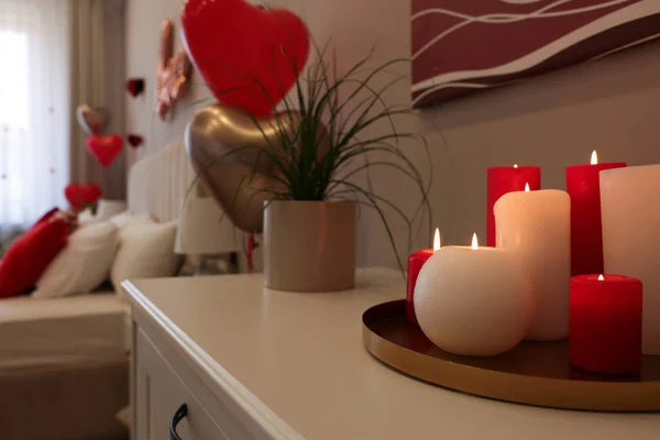 Burning candles on white table in room decorated for Valentine\'s Day