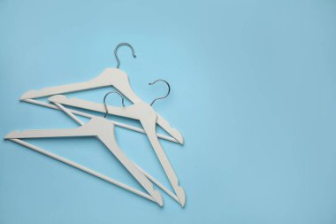 Boş elbise askıları açık mavi arka planda, düz yerde. Metin için boşluk