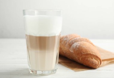 Beyaz ahşap masada lezzetli latte macchiato ve kruvasan.