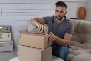 Evdeki paketi açmak için bıçak kullanan bir adam.