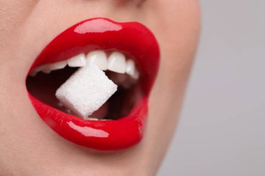 Güzel dudakları olan, açık gri arka planda küp şeker yiyen genç bir kadının yakın görüntüsü.