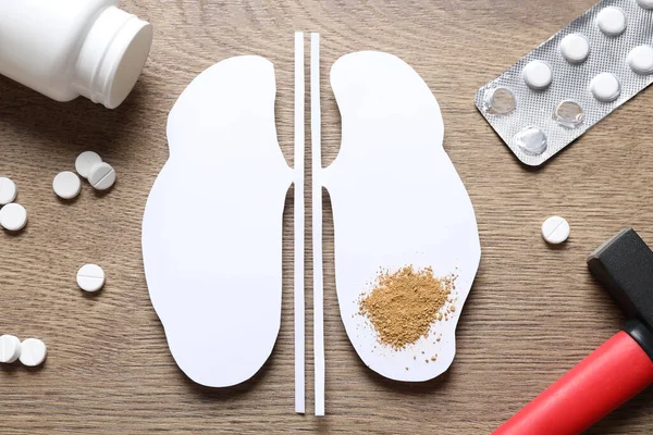 Paper cutout with sand, pills and hammer on wooden table, flat lay. Kidney stone disease