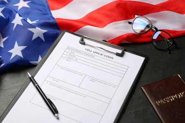 Amerikan bayrağı, vize başvuru formu, pasaport ve gözlükler siyah masada.
