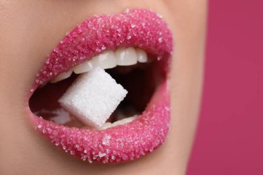 Güzel dudakları olan, pembe arka planda küp şeker yiyen gençlerin yakın görüntüsü