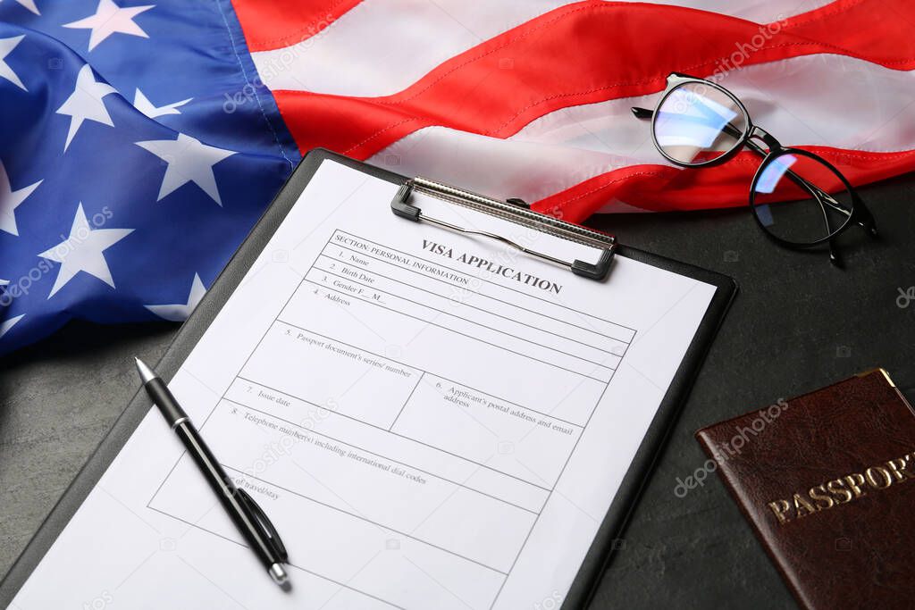American flag, visa application form, passport and glasses on black table