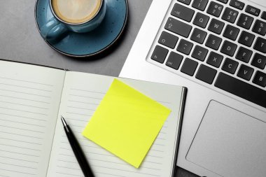 Laptop, planlayıcı, boş yapışkan not, gri masaya bir fincan kahve ve kalem, düz konum. Tasarım için boşluk