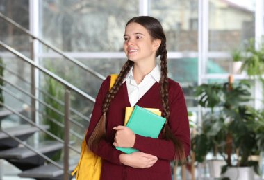 Okul üniformalı, içinde kitap ve sırt çantası olan genç bir kız.