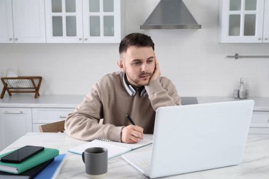Genç adam mutfakta çalışmak için modern dizüstü bilgisayar kullanıyor. Uzaklık öğrenimi