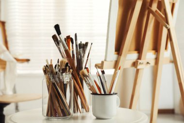 Stüdyodaki beyaz masada farklı boya fırçaları olan tutucular. Sanatçının işyeri