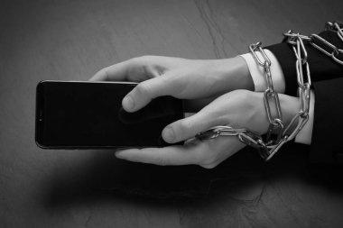 Zincire vurulmuş elleri kara masada akıllı telefon kullanan internet bağımlısı kadının yakın görüntüsü, mesaj için yer. Siyah ve beyaz etkisi