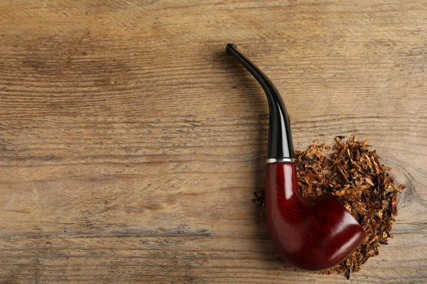 Smoking pipe with tobacco on wooden table, flat lay. Space for text