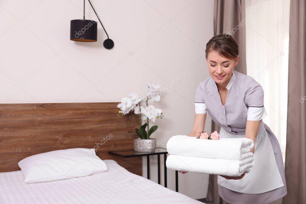 Beautiful chambermaid putting fresh towels on bed in hotel room