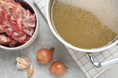 Lezzetli kemik suyu ve malzemelerle dolu tencere, açık gri masa, düz uzanmış