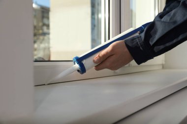 İnşaat işçisi caulk ile pencereyi kapatıyor.