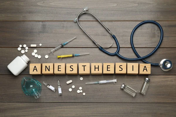 Düz kompozisyon, tahta masanın üzerinde küp ve uyuşturucudan yapılmış anestezi sözcüğüyle.