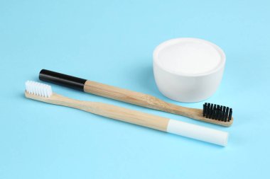 Bambu diş fırçaları ve açık mavi arka planda kabartma tozu içeren kase.